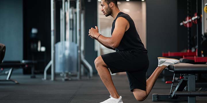 A man performing a Bulgarian split squat in a gym.