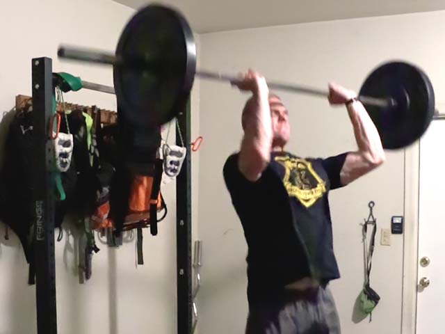 Reaching the top of the squat press, and beginning to press the barbell off the shoulders.