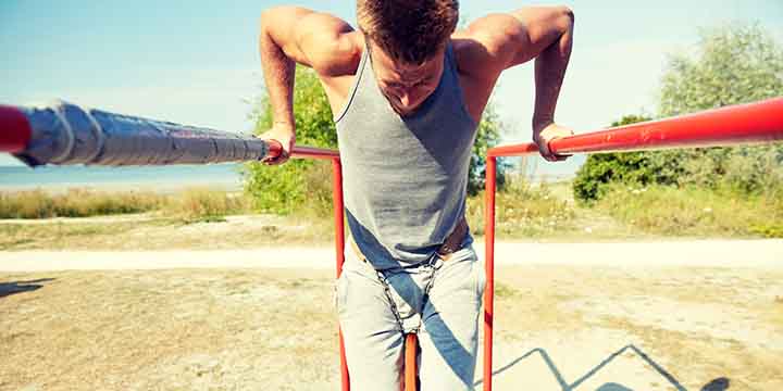 A man does weighted dips outdoors on a set of parallel bars.