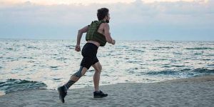 A man running with a weighted vest on a beach.