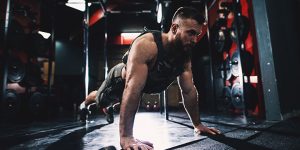 A man in a weight vest doing push-ups in a CrossFit gym.