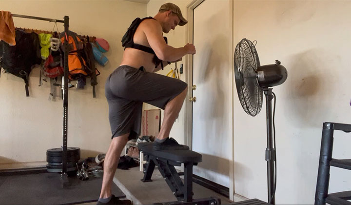 The author of Lunch Break Fitness performing step-ups in a weighted vest onto a 20" bench with his right leg.